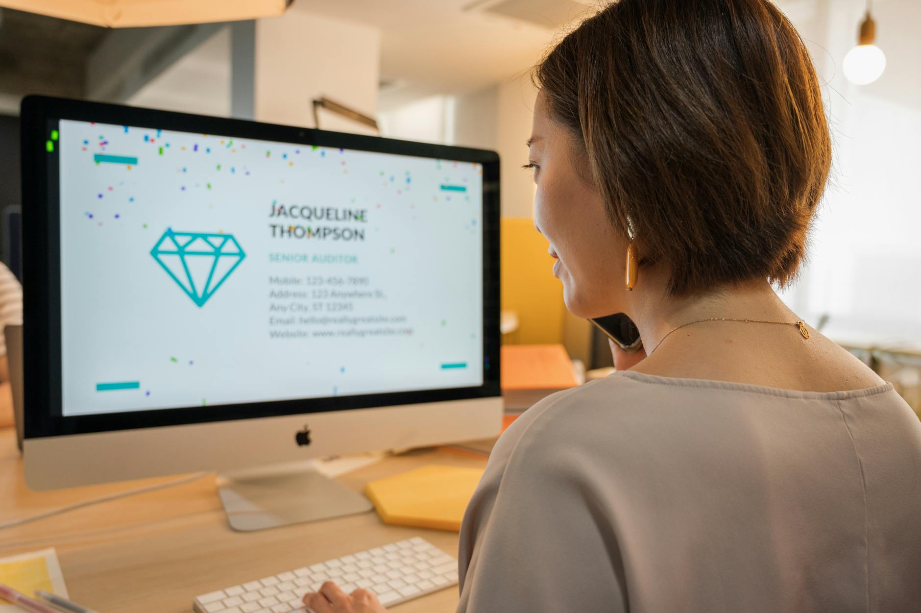 woman wearing jewelry and beige shirt in front of silver imac computer with jewelry content on it